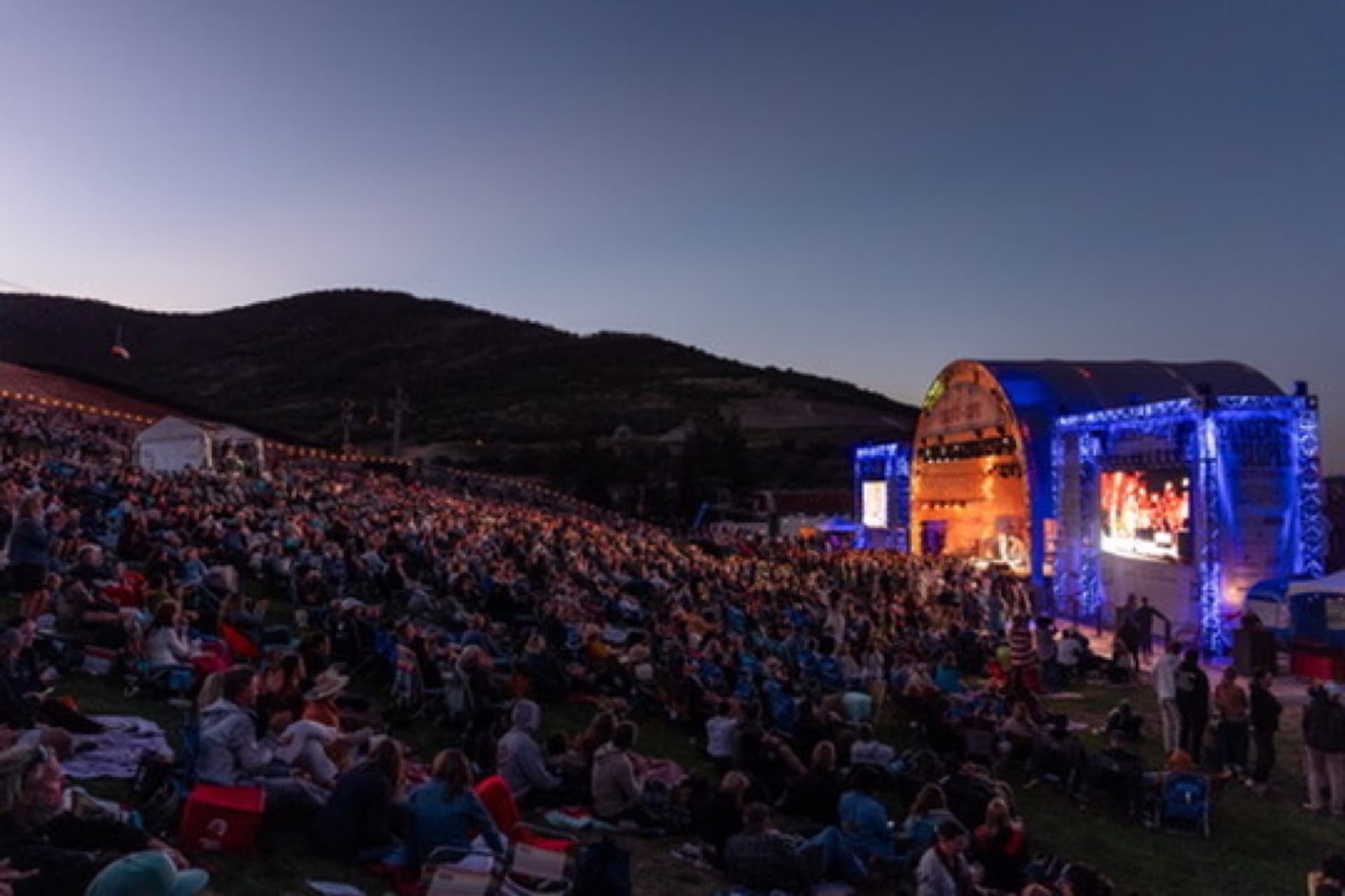 Concert on the Slopes outdoor stage glowing at dusk with a large hillside audience.